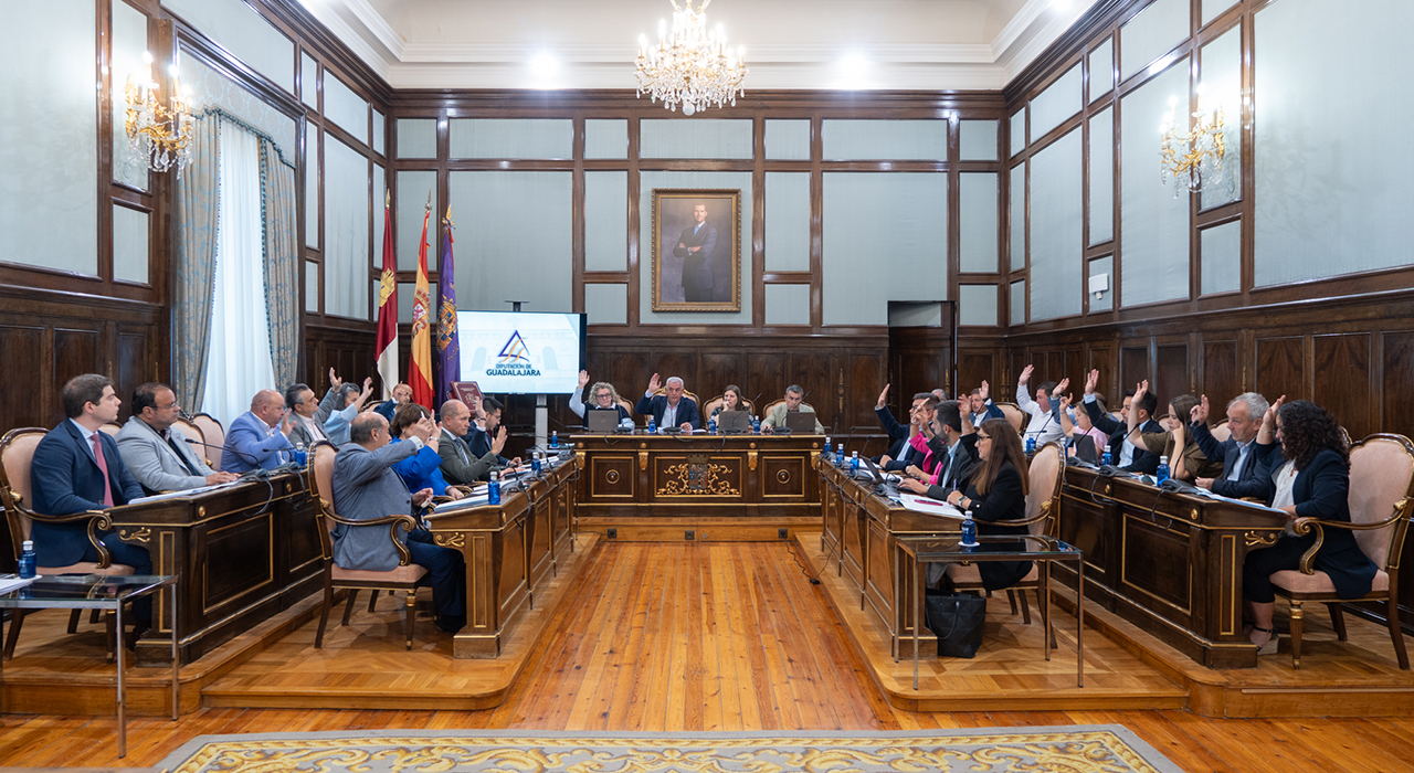 La Diputación traspasa a los ayuntamientos de El Casar y Azuqueca los tramos urbanos de dos carreteras 2 Los tramos de las carreteras provinciales GU-193 y GU-103 que discurren por los cascos urbanos de El Casar y de Azuqueca de Henares, respectivamente, pasarán a ser de titularidad municipal. El pleno de la Diputación de Guadalajara, actualmente titular de la totalidad de los trazados de ambas carreteras, ha aprobado en pleno las mutaciones demaniales subjetivas de ambas travesías a favor de los ayuntamientos de El Casar y de Azuqueca de Henares.El acuerdo del pleno de la Diputación se ha adoptado por unanimidad de todos los grupos políticos y responde a la voluntad expresada por ambos ayuntamientos de hacerse cargo de la titularidad de los tramos viales o travesías que pasan por sus respectivos cascos urbanos.Tanto el Ayuntamiento de El Casar como el de Azuqueca de Henares deberán ahora ratificar por acuerdo de sus respectivos plenos municipales la aceptación del cambio de titularidad del vial que afecta a cada uno de ellos para posteriormente firmar sendos convenios con la Diputación de Guadalajara.Cada uno de estos convenios establece que la Diputación ejecutará las actuaciones de adecuación necesarias para la transformación de cada tramo en vial urbano y, a partir de entonces, el Ayuntamiento asume todas las competencias inherentes a la conservación, mantenimiento, explotación, disciplina y gestión del tramo cedido. Para la transformación de los tramos en viales urbanos, los ayuntamientos deberán facilitar la disponibilidad de los espacios necesarios para la ejecución de las actuaciones y ejecutar previamente las canalizaciones o infraestructuras que resulten necesarias antes de las obras de acondicionamiento.1,3 km y 9.114 metros cuadrados afectados en El Casar.
La carretera GU-193 es la vía provincial que va desde la carretera N-320 hasta el límite provincial por El Casar. El tramo cuya titularidad va a pasar de provincial a municipal es el que comprende el recorrido existente desde la intersección con la carretera N-320 hasta el inicio de la rotonda de acceso al centro de salud de la localidad.Este tramo tiene una longitud total de 1.323,70 metros y una superficie de 9.114 metros cuadrados. El servicio de Infraestructuras de la Diputación ha redactado el proyecto de actuación para acondicionar este tramo como vial urbano, en el que se definen técnica y económicamente las obras de adecuación que la propia Institución Provincial llevará a cabo.Dichas actuaciones para adaptar el tramo a su nueva funcionalidad urbana consistirán en: fresado y extendido de nueva capa de rodadura, repintado de marcas y símbolos viales y cerramiento de la rotonda del centro de salud mediante bordillo, capa de adoquín perimetral, acabado interior de rocalla, colocación de dos puntos de luz, plantación de dos árboles, instalación de captafaros LED solares en bordillos interiores y mejora de señalización de seis pasos de peatones.1,15 km y 20.072,74 metros cuadrados en Azuqueca.
En el caso de Azuqueca de Henares, la carretera provincial GU-103 es la que sale desde la GU-102 y lleva al límite de la provincia de Guadalajara y a Meco. El tramo cuya titularidad cede la Diputación al Ayuntamiento azudense es el comprendido entre la Avenida de Alcalá y el cruce con la calle Rafael Guijosa de la localidad, mientras que el tramo situado desde ese punto hasta el límite de la provincia seguirá siendo de titularidad provincial.Al igual que en El Casar, la Diputación se hará cargo de la adaptación del tramo afectado como vial urbano ejecutando el proyecto que ha elaborado el servicio provincial de Infraestructuras. De esta forma, en los 1.156,12 metros de longitud y 20.072 metros cuadrados de superficie que pasan a ser de titularidad municipal, la Diputación llevará a cabo las siguientes actuaciones: fresado y extendido de nueva capa de rodadura, repintado de marcas y símbolos viales, adecuación del interior de la rotonda de enlace con la calle Rafael Guijosa mediante cerco de adoquín, relleno del interior con sistema drenante y marmolina blanca, plantación de magnolio y señalización de todas las rotondas cedidas con catadióptricos leds solares.