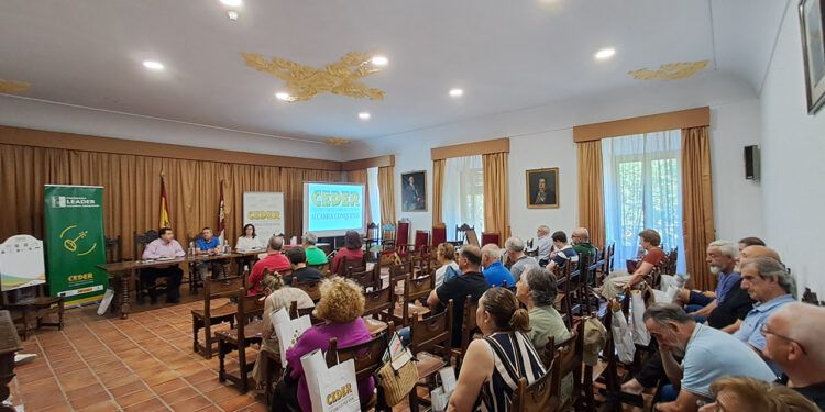 Nueva inyección de 275.000 euros para impulsar autónomos y pymes en la Alcarria Conquense 1 La Asociación CEDER Alcarria Conquense ha celebrado su Asamblea General Ordinaria en el histórico edificio del antiguo Convento de la Merced de Huete. Durante este encuentro, la directiva ha dado luz verde a una nueva convocatoria de ayudas dotada con 275.000 euros. Esta partida económica, que se publicará en las próximas semanas, servirá de respaldo directo para los proyectos de autónomos, empresas e industrias agroalimentarias instaladas en la comarca. El encuentro, dirigido por el presidente Juan Carlos Bermejo junto al alcalde optense Francisco Javier Doménech y la gerente Clara Isabel Fernández-Cabrera, sirvió también para aprobar las cuentas del pasado ejercicio 2025. La gerencia expuso el balance definitivo de la Medida 19 LEADER, un programa que se cerró el año pasado dejando en el territorio 174 proyectos ejecutados. Esta iniciativa movilizó 6,5 millones de euros en ayudas que se tradujeron en una inversión real de 9,3 millones para los pueblos de la zona. Respecto al plan actual PEPAC 2023-2027, la asociación ya ha resuelto cuatro convocatorias. Estos fondos recientes han permitido a emprendedores locales iniciar su actividad y a distintos ayuntamientos adquirir nueva maquinaria o mejorar sus infraestructuras de promoción cultural. Proyectos para la comarca La asamblea detalló varias iniciativas de promoción territorial ejecutadas en los últimos meses y avanzó las líneas de trabajo futuro con el apoyo de la Diputación de Cuenca: Creación de una aplicación móvil con seis rutas audioguiadas por los espacios de la Red Natura 2000 Implantación de una plataforma de inteligencia artificial diseñada para negocios comarcales Formación técnica para alcaldes y trabajadores municipales sobre licencias y contratación Continuidad de los murales creativos "Pintando Recuerdos" en las fachadas de los pueblos Organización de la VI Feria de Oficios y Tradiciones que acogerá Tinajas el 25 de julio Próxima redacción de la Agenda de Desarrollo Rural de la zona y renovación de la señalización territorial Evolución del desarrollo rural El archivo de Liberal de Castilla permite comprobar cómo la estrategia de CEDER Alcarria Conquense ha ido evolucionando en el último año hacia un modelo de dinamización mucho más tecnológico e itinerante. La llegada de la Feria de Oficios a Tinajas este mes de julio consolida el sistema de rotación de sedes que ya funcionó con éxito en la edición del verano pasado, garantizando que el impacto económico de estos eventos repueble temporalmente distintos municipios cada año. Por otro lado, la confirmación de la continuidad del programa "Pintando Recuerdos" demuestra el asentamiento de una idea que comenzó como una intervención aislada para rescatar palabras en desuso y se ha convertido en una seña de identidad visual de la comarca. Este enfoque artístico, sumado al salto digital que suponen las nuevas rutas audioguiadas, refleja un cambio claro en la lucha contra la despoblación: los fondos europeos ya no solo construyen infraestructuras físicas, sino que generan nuevos reclamos turísticos adaptados al perfil del visitante actual.