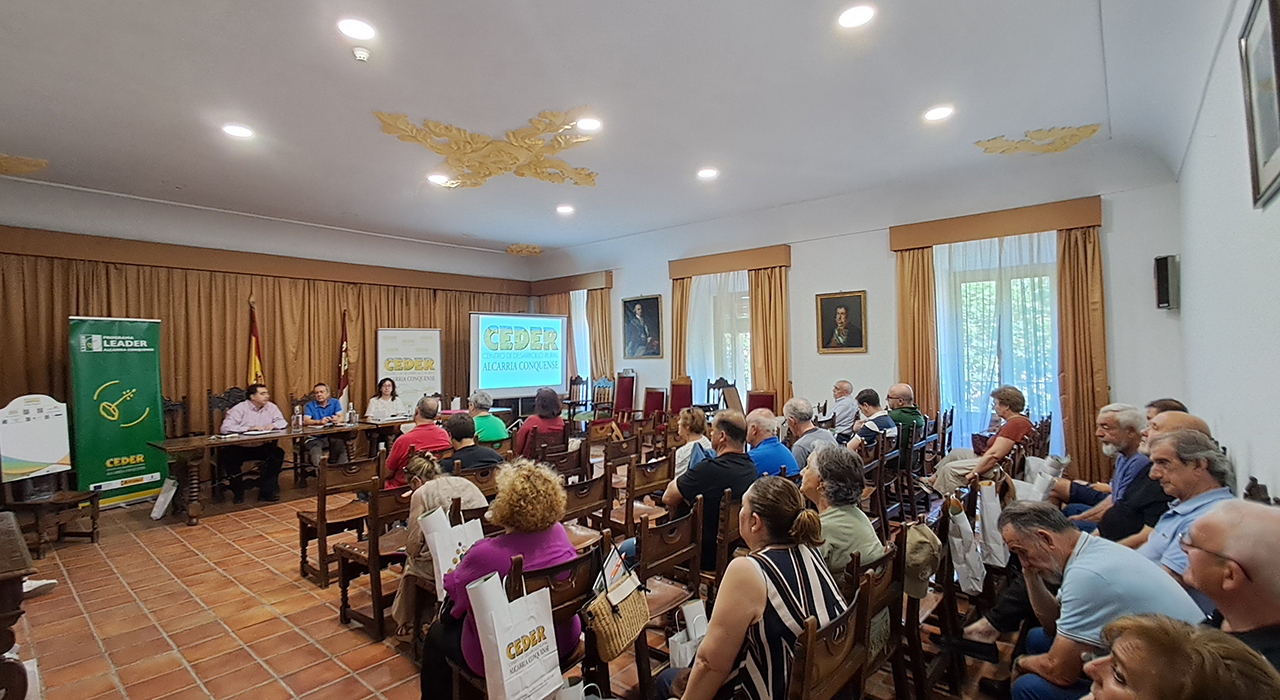 Nueva inyección de 275.000 euros para impulsar autónomos y pymes en la Alcarria Conquense 2 La Asociación CEDER Alcarria Conquense ha celebrado su Asamblea General Ordinaria en el histórico edificio del antiguo Convento de la Merced de Huete. Durante este encuentro, la directiva ha dado luz verde a una nueva convocatoria de ayudas dotada con 275.000 euros. Esta partida económica, que se publicará en las próximas semanas, servirá de respaldo directo para los proyectos de autónomos, empresas e industrias agroalimentarias instaladas en la comarca.El encuentro, dirigido por el presidente Juan Carlos Bermejo junto al alcalde optense Francisco Javier Doménech y la gerente Clara Isabel Fernández-Cabrera, sirvió también para aprobar las cuentas del pasado ejercicio 2025. La gerencia expuso el balance definitivo de la Medida 19 LEADER, un programa que se cerró el año pasado dejando en el territorio 174 proyectos ejecutados. Esta iniciativa movilizó 6,5 millones de euros en ayudas que se tradujeron en una inversión real de 9,3 millones para los pueblos de la zona.Respecto al plan actual PEPAC 2023-2027, la asociación ya ha resuelto cuatro convocatorias. Estos fondos recientes han permitido a emprendedores locales iniciar su actividad y a distintos ayuntamientos adquirir nueva maquinaria o mejorar sus infraestructuras de promoción cultural.Proyectos para la comarca
La asamblea detalló varias iniciativas de promoción territorial ejecutadas en los últimos meses y avanzó las líneas de trabajo futuro con el apoyo de la Diputación de Cuenca:Creación de una aplicación móvil con seis rutas audioguiadas por los espacios de la Red Natura 2000Implantación de una plataforma de inteligencia artificial diseñada para negocios comarcalesFormación técnica para alcaldes y trabajadores municipales sobre licencias y contrataciónContinuidad de los murales creativos "Pintando Recuerdos" en las fachadas de los pueblosOrganización de la VI Feria de Oficios y Tradiciones que acogerá Tinajas el 25 de julioPróxima redacción de la Agenda de Desarrollo Rural de la zona y renovación de la señalización territorialEvolución del desarrollo rural
El archivo de Liberal de Castilla permite comprobar cómo la estrategia de CEDER Alcarria Conquense ha ido evolucionando en el último año hacia un modelo de dinamización mucho más tecnológico e itinerante. La llegada de la Feria de Oficios a Tinajas este mes de julio consolida el sistema de rotación de sedes que ya funcionó con éxito en la edición del verano pasado, garantizando que el impacto económico de estos eventos repueble temporalmente distintos municipios cada año.Por otro lado, la confirmación de la continuidad del programa "Pintando Recuerdos" demuestra el asentamiento de una idea que comenzó como una intervención aislada para rescatar palabras en desuso y se ha convertido en una seña de identidad visual de la comarca. Este enfoque artístico, sumado al salto digital que suponen las nuevas rutas audioguiadas, refleja un cambio claro en la lucha contra la despoblación: los fondos europeos ya no solo construyen infraestructuras físicas, sino que generan nuevos reclamos turísticos adaptados al perfil del visitante actual.