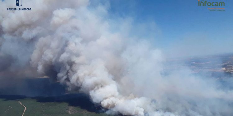 Confinan Almiruete y Palancares mientras el incendio de La Mierla eleva a tres los núcleos evacuados 1 La evolución del incendio forestal originado en La Mierla mantiene el Nivel 2 de emergencia y ha obligado a tomar nuevas medidas drásticas de protección ciudadana durante las últimas horas. Las autoridades han ordenado el confinamiento estricto de las poblaciones de Almiruete y Palancares, instruyendo a todos los vecinos a permanecer en el interior de los edificios y mantener cerradas puertas y ventanas para evitar la intoxicación por humo. Estas dos localidades se suman a la zona del embalse de Beleña, que ya se encontraba bajo esta misma restricción perimetral. Paralelamente, el avance de las llamas por la masa arbolada ha forzado a actualizar la lista de municipios desalojados. A los vecinos de La Mierla y a los menores del campamento de Umbralejo, evacuados durante la tarde de ayer, se suma ahora la población de Muriel, que pasa de estar confinada a ser evacuada por completo. El fuego, detectado originalmente a las 13:55 horas del 16 de julio por un vigilante fijo, exige un esfuerzo técnico y humano sin precedentes recientes en la zona. A primera hora de esta mañana, combaten el siniestro sobre el terreno 171 profesionales apoyados por 22 medios terrestres y de coordinación, a la espera de que la visibilidad y las condiciones permitan la reincorporación de los medios aéreos. En el cómputo global de la emergencia, el operativo ha llegado a desplegar a 336 personas y 70 medios, incluyendo 17 aeronaves, para tratar de contener el perímetro. Estrategias de protección civil Consultando la hemeroteca de Liberal de Castilla sobre la gestión de grandes incendios en la comarca de la Arquitectura Negra, la combinación simultánea de órdenes de confinamiento y evacuación responde a un protocolo técnico muy definido. Históricamente, la orografía de la Sierra Norte de Guadalajara impone retos severos para el movimiento masivo de personas a través de sus estrechas carreteras comarcales. La doctrina actual del operativo diferencia claramente el tipo de riesgo para aplicar una medida u otra. La evacuación de La Mierla o Muriel se ejecuta cuando el avance del frente de llamas o la carga térmica amenazan directamente las viviendas. Por el contrario, el confinamiento decretado hoy para Almiruete y Palancares busca proteger las vías respiratorias de la población frente a columnas de humo densas y cambios erráticos del viento. Encerrar a los vecinos en sus casas evita colapsar las vías de comunicación, garantizando que el medio centenar de camiones y vehículos pesados de extinción puedan transitar libremente hacia la zona cero del fuego.