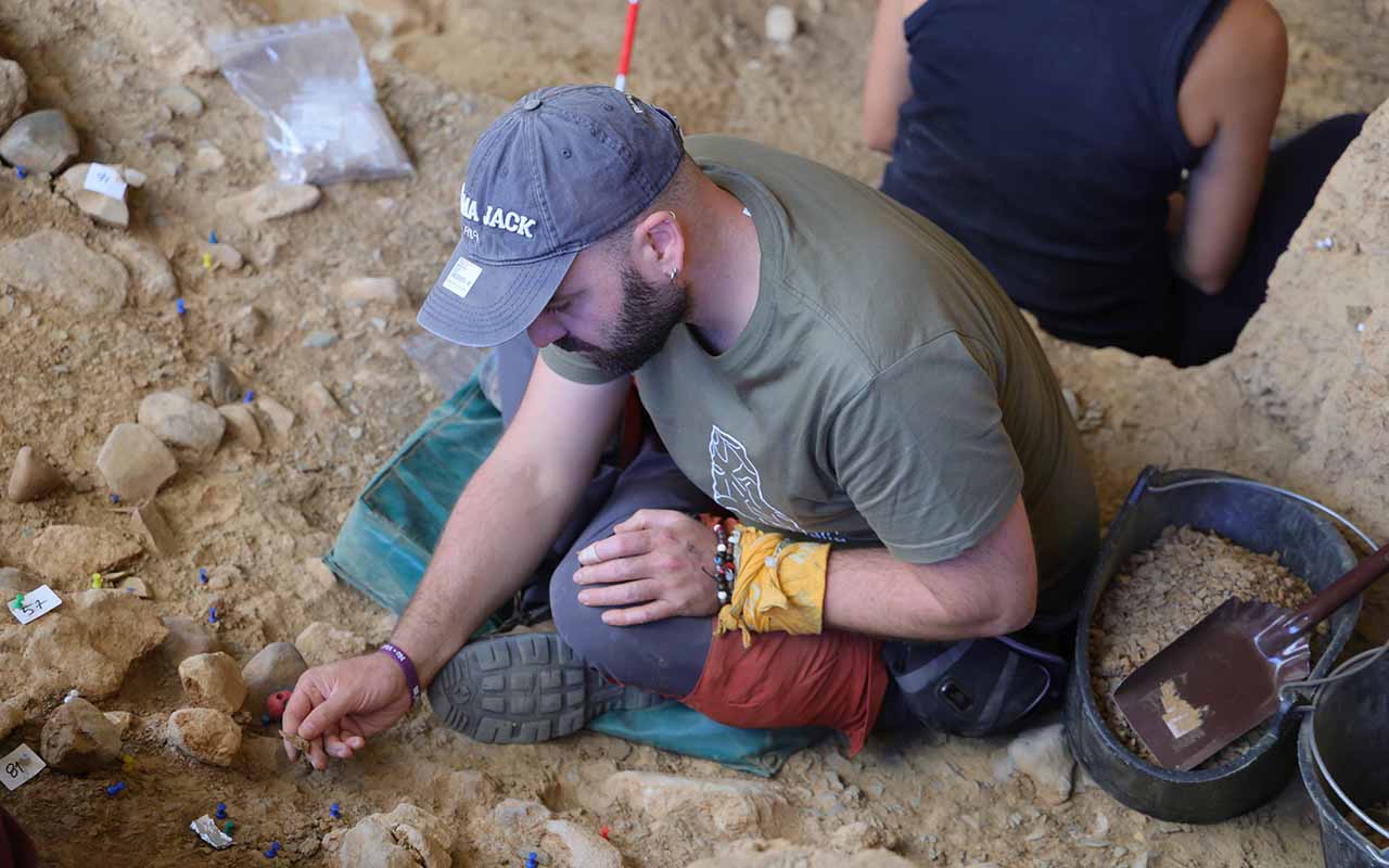 Un equipo multidisciplinar compuesto por quince especialistas acaba de concluir la novena campaña sistemática de excavaciones en el abrigo de La Malia, en Tamajón. Durante estos trabajos, codirigidos por el investigador Adrián Pablos y enmarcados en el proyecto PYHIP-Tamajón, se han recuperado nuevas herramientas de piedra, restos de carbón y huesos de animales consumidos por los grupos humanos que habitaron esta zona de Guadalajara hace más de 30.000 años. El objetivo de la intervención es documentar cómo vivían, se adaptaban y utilizaban el territorio estas poblaciones nómadas paleolíticas.Durante la temporada de 2026 los arqueólogos no han extraído una pieza única de carácter excepcional, sino un conjunto de elementos cotidianos vinculados a antiguas hogueras y zonas de procesado de alimentos. Los investigadores continúan excavando hacia niveles más profundos para intentar determinar el origen exacto de las ocupaciones, manteniendo abierta la hipótesis de alcanzar en el futuro estratos correspondientes a los neandertales.El desarrollo de este proyecto científico mantiene además un fuerte vínculo social con el municipio, especialmente tras el reciente incendio forestal que ha afectado al entorno de la localidad. Los investigadores han trasladado al Ayuntamiento de Tamajón su disposición para colaborar en la recuperación y dinamización de la zona, una vocación pública que ya se materializó a principios de septiembre con unas jornadas de puertas abiertas que reunieron a más de un centenar de personas en el propio yacimiento.La evolución de las investigaciones en La Malia ha transformado por completo la concepción histórica del centro de la Península, considerado durante años una "tierra de nadie". Desde el inicio de las excavaciones en 2018, los descubrimientos han situado a Tamajón en el mapa científico internacional. El verdadero punto de inflexión se produjo en 2024, cuando la revista Science Advances fechó las ocupaciones humanas de este abrigo entre hace 36.200 y 31.760 años. A esto se sumaron estudios posteriores en 2025 que identificaron estrategias de caza recurrentes y los restos de ADN más antiguos del linaje ibérico de caballos. Toda esta trayectoria de descubrimientos revierte directamente en el territorio a través del Centro de Interpretación Paleontológica y Arqueológica de Tamajón (CIPAT), inaugurado en 2021 y reconocido con el Premio Regional de Turismo Sostenible, consolidando la herencia prehistórica como un motor cultural y educativo para la Sierra Norte.